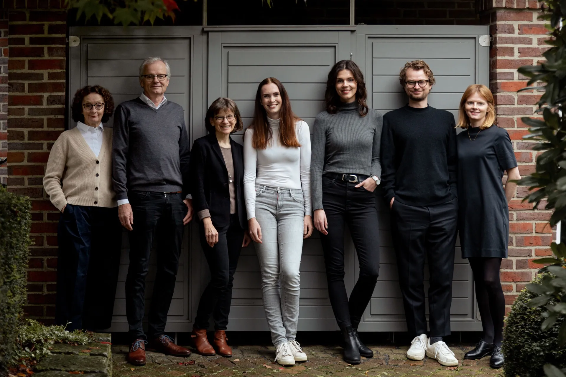 Das Team von Schewe Architektur vor einer Backsteinfassade mit grauem Holztor
